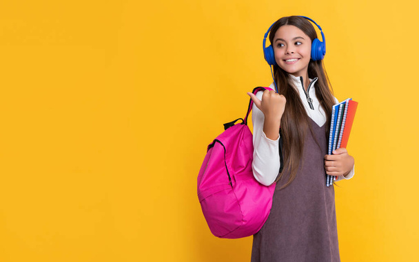 happy girl in headphones with school backpack with workbook on yellow background. - Valokuva, kuva