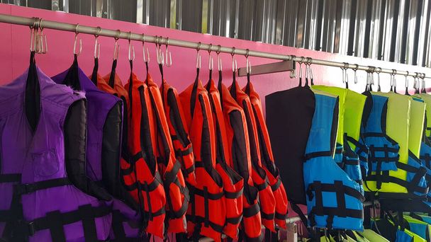 Many purple or violet, red, blue and green life jacket hanging on stainless steel hanger for people or group of tourist rent and wear for safety when take a boat or speed boat on sea or ocean.  - Photo, Image