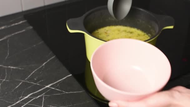 jonge vrouw kok gieten hete soep van steelpan in kom voor lunch thuis - Video