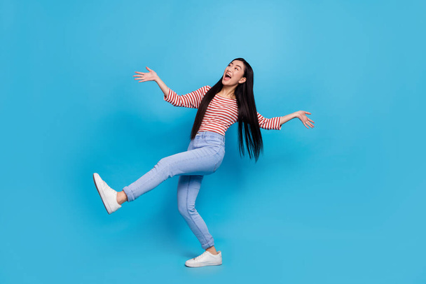 Full length photo of excited pretty woman wear striped shirt dancing looking empty space isolated blue color background. - Fotó, kép