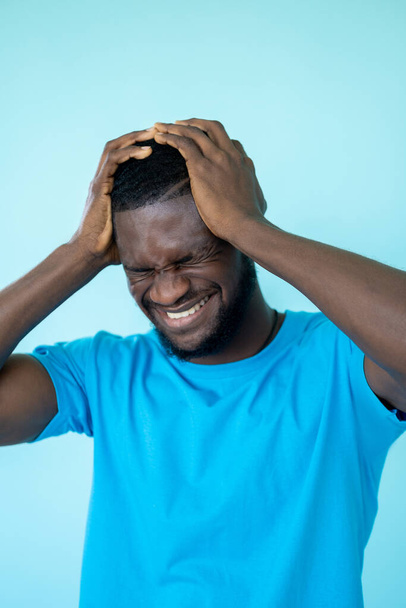 Headache pain. Stress pressure. Depression problem. Suffering frustrated man holding head in migraine ache isolated on blue background. - Photo, image