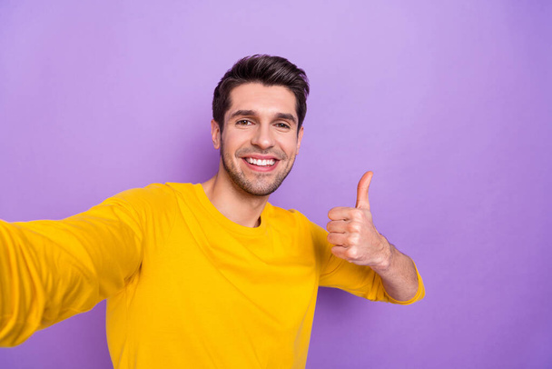 Photo of cheerful toothy beaming male take selfie show thumb-up recommend product isolated on purple color background. - Фото, зображення