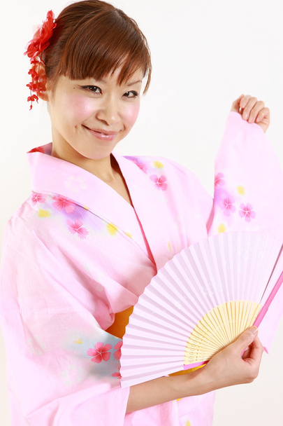 Young woman wearing Japanese kimono with paper fan - 写真・画像