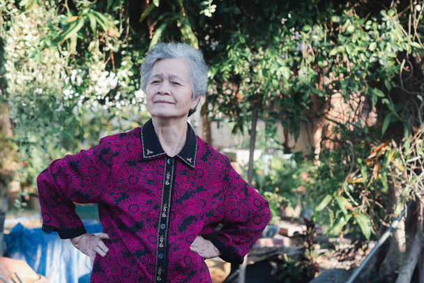 Старшая женщина с короткими белыми волосами, улыбающаяся, смотрящая в камеру, и упражнения, стоя в саду. Пространство для текста. Концепция пожилых людей и здравоохранения. - Фото, изображение