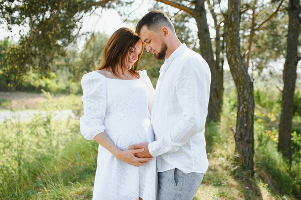 Happy and young pregnant couple hugging in nature. - Foto, Bild
