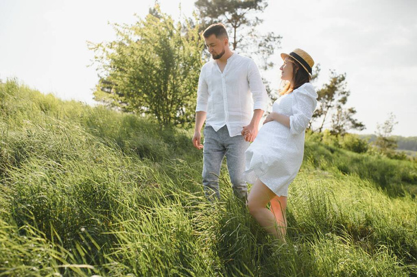 Happy and young pregnant couple hugging in nature. - Foto, Bild