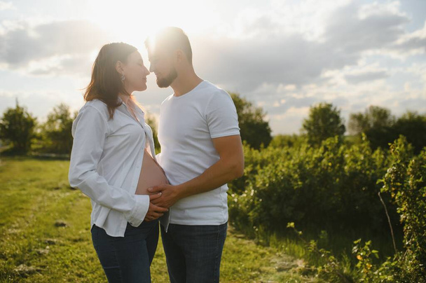 Happy and young pregnant couple hugging in nature. - Photo, Image
