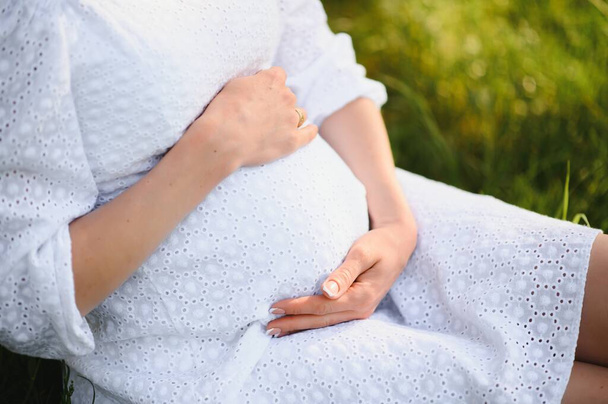 Close-up of pregnant woman with hands on her belly on nature background - Foto, Imagem