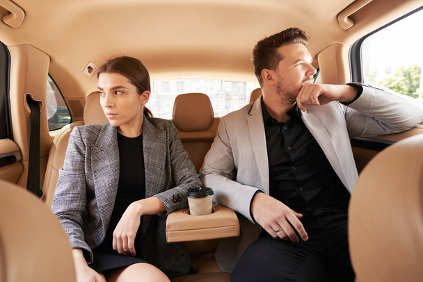 Ernsthafte Arbeitskollegen sitzen bei Dienstreise im Auto nebeneinander - Foto, Bild