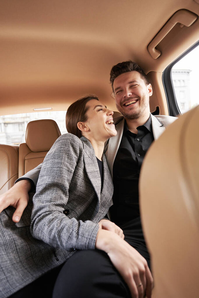 車の後部座席に座っている間に陽気なビジネスマンの巨大な女性と笑顔 - 写真・画像