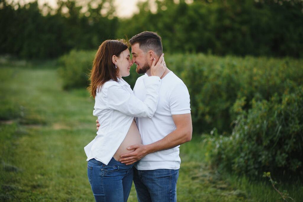 Happy and young pregnant couple hugging in nature. - Photo, image