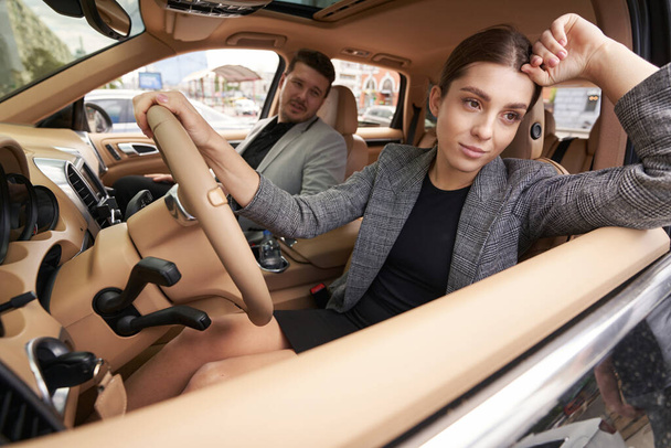 Frau sitzt mit der Hand am Lenkrad auf dem Fahrersitz und schaut aus dem Autofenster, während sie Meinungsverschiedenheiten mit ihrem Mann hat - Foto, Bild