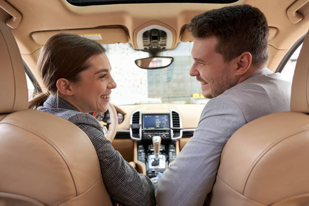 Cheerful lady looking at gentleman and smiling while sitting on driver seat in car - Photo, Image