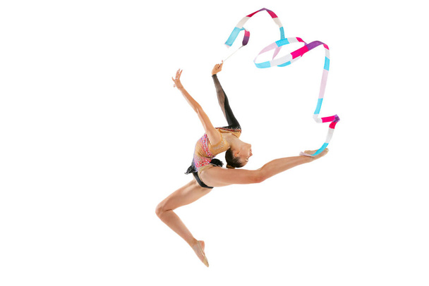 Flying with multicolored ribbon. Portrait of young sportive girl, rhythmic gymnastics artist isolated on white studio background. Concept of sport, action, aspiration, education, active lifestyle - Φωτογραφία, εικόνα