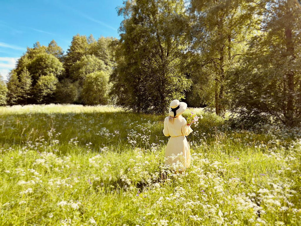  Hasır şapkalı, çiçekli vahşi kadınlar güneşli bir günde ormanda yürür. Mavi gökyüzü manzarası.  - Fotoğraf, Görsel