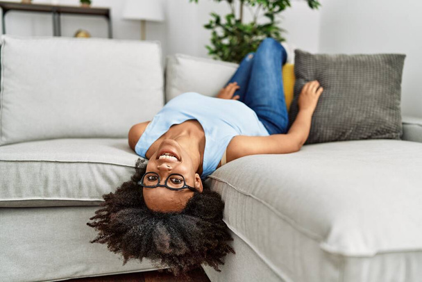 Молодая африканская американка, уверенно улыбающаяся, лежа дома на диване - Фото, изображение