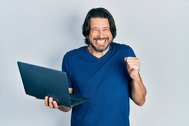 Middle age caucasian man working using computer laptop screaming proud, celebrating victory and success very excited with raised arm  - Photo, Image