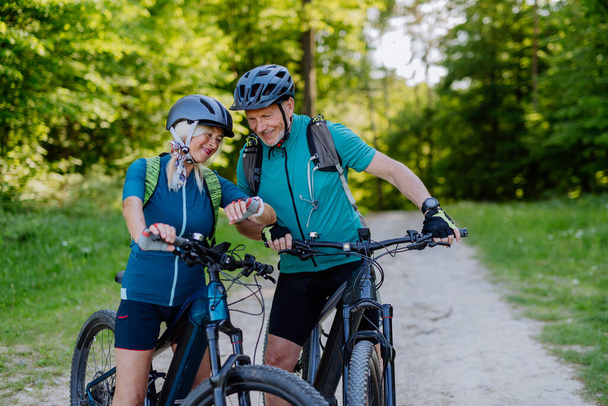 A portrait of active senior couple riding bicycles at summer park, looking at sports smartwatch, checking their performance. - Fotoğraf, Görsel