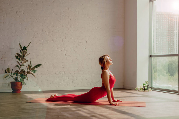 Güneş selamı. Kırmızı spor tulumlu genç kadın yoga stüdyosunda yoga yapıyor. Sağlıklı bir yaşam tarzı. Yüksek kalite fotoğraf - Fotoğraf, Görsel