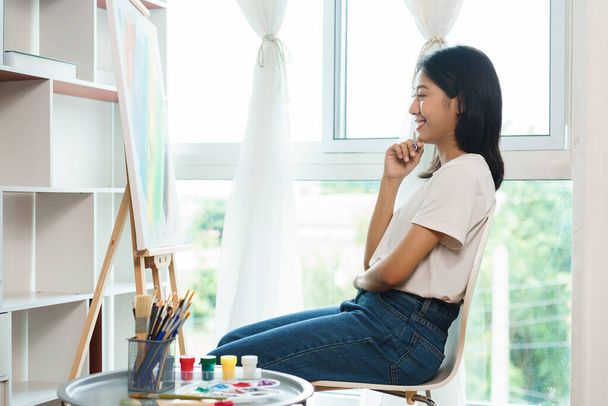 アジアの女性アーティストがキャンバスの前に座り、アートワークのアイデアを生み出そうと考えています。. - 写真・画像