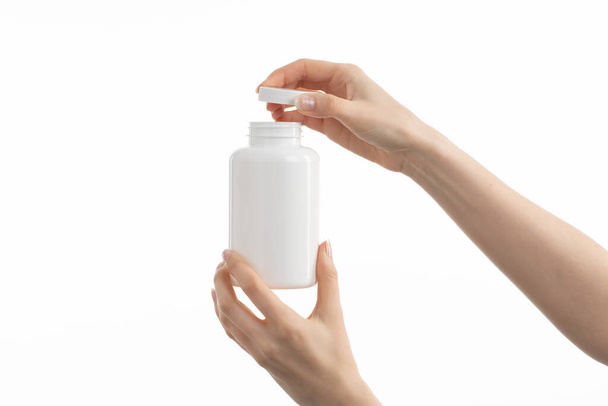 Immagine ravvicinata di una donna con in mano una bottiglia bianca di pillole o vitamine o integratori. - Foto, immagini