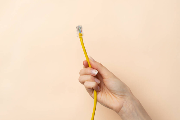 Close up image of woman's hand holding a yellow cable. She don`t know how to connect computer to the internet instead of a wifi connection - Zdjęcie, obraz