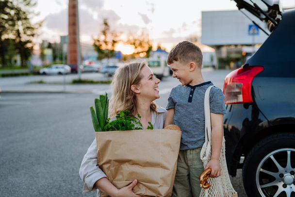 A young mother with little son after shopping holding zero waste shopping bags with grocery near car. - Zdjęcie, obraz
