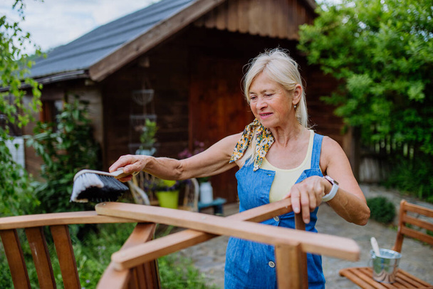 A senior woman cleaning garden furniture and getting the garden ready for summer - Foto, afbeelding