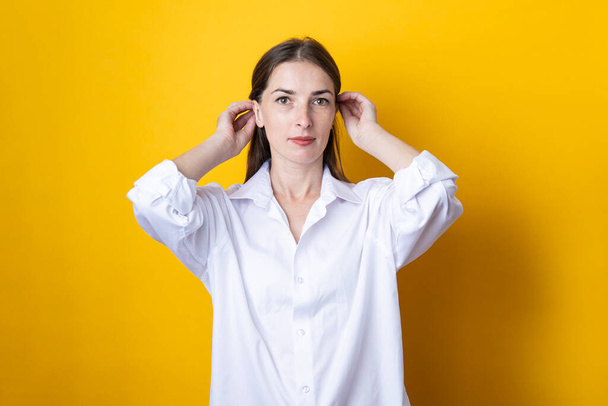 Young woman in a white shirt straightens her hair on a yellow background. - Photo, Image