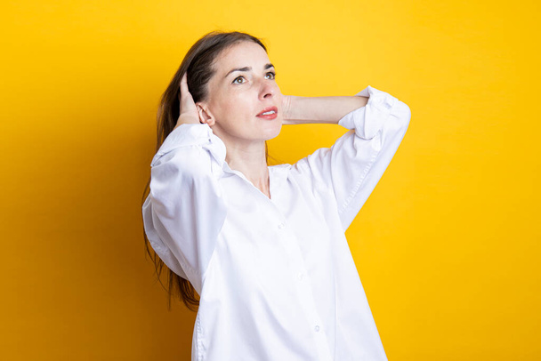 Jeune femme dans une chemise blanche redresse ses cheveux sur un fond jaune. - Photo, image
