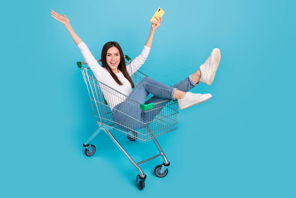 Photo of good mood overjoyed playful lady blogger influencer sit in pushcart isolated on blue color background. - Φωτογραφία, εικόνα
