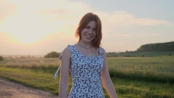 Fröhliches Mädchen mit roten Haaren und Sommersprossen in einem Sommerkleid, das herumtanzt, Spaß hat und bei Sonnenuntergang auf der Straße verspielt flirtet - Filmmaterial, Video