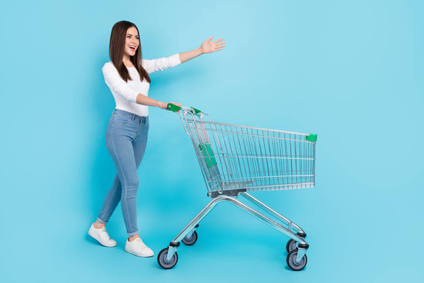 Photo of excited funky young woman wear white shirt walking shopping tray looking empty space isolated blue color background. - Fotó, kép