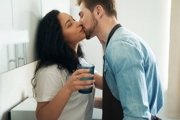 Man in love giving kiss to young female seated on kitchen counter - 写真・画像
