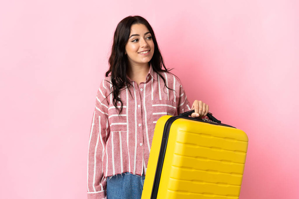 Молодая белая женщина изолирована на розовом фоне в отпуске с чемоданом - Фото, изображение