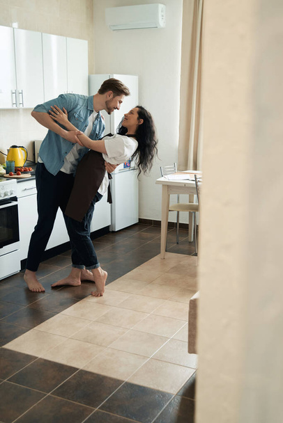 Smiling man in love dancing with his happy young woman in kitchen - Фото, зображення