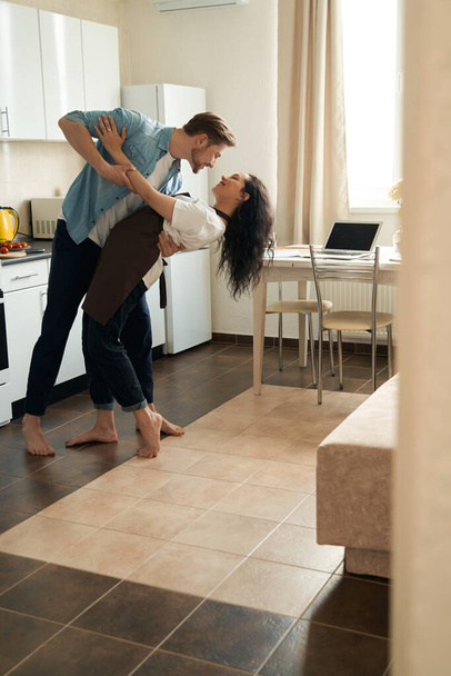 Passionate young male and his smiling beloved woman performing tango in kitchen - 写真・画像