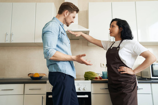Upset young woman pushing away sad guy during their quarrel in kitchen - Foto, Imagem
