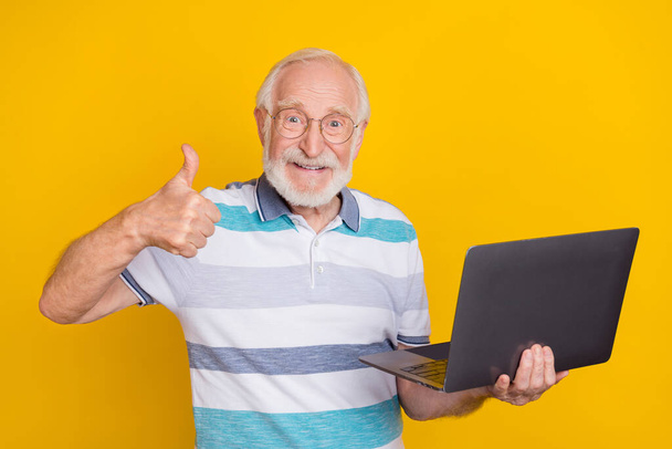 Portrait of attractive cheerful intellectual grey haired man using laptop showing thumbup isolated over bright yellow color background. - Фото, зображення