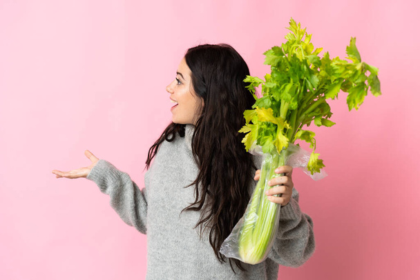 Young caucasian woman holding a celery isolated on blue background with surprise facial expression - Фото, зображення