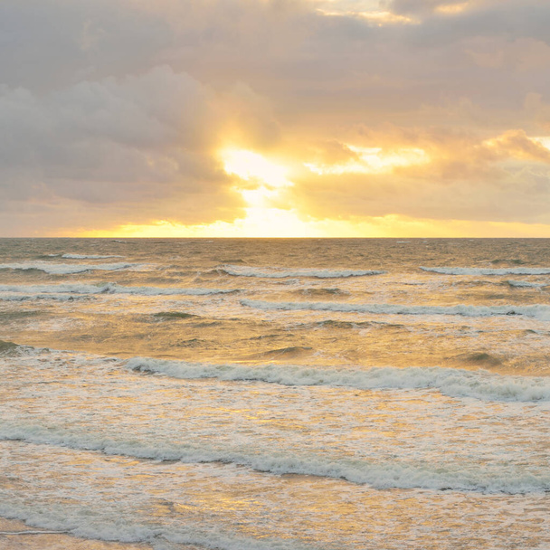 Blick von der Ostseeküste bei Sonnenuntergang. Dramatische Wolkenlandschaft, glühende Wolken, goldenes Sonnenlicht nach dem Sturm. Natur, Umwelt, Klimawandel, unbeständiges Wetter - Foto, Bild