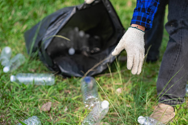 Młody człowiek zbiera plastikowe butelki i czarne torby i zbiera je razem, aby sprzedać je kupującym, którzy zbierają je do recyklingu. Pojęcie separacji odpadów i ochrony środowiska - Zdjęcie, obraz