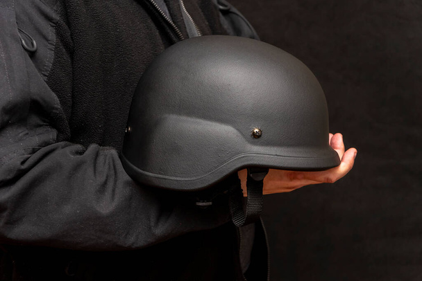 A military man holds an army helmet in his hand, black background. Concept: volunteer at war, war in Ukraine, civil self-defense, army unit. - Fotografie, Obrázek
