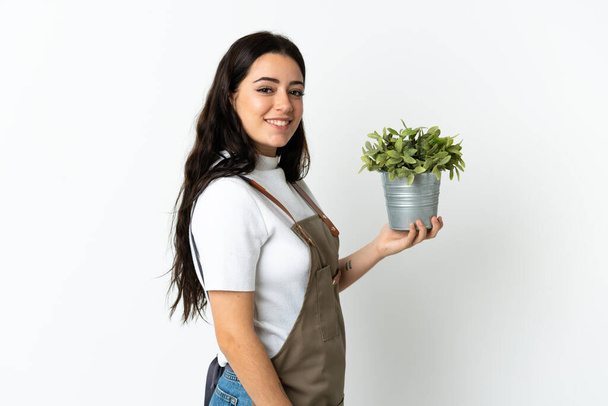 Giovane donna caucasica che tiene una pianta isolata su sfondo bianco sorridendo molto - Foto, immagini