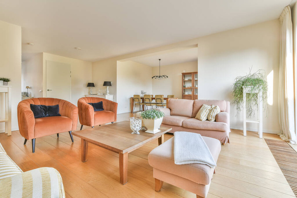 Table en bois minable avec chaises et vase situé près du canapé confortable contre les murs clairs avec des décorations dans un appartement moderne - Photo, image
