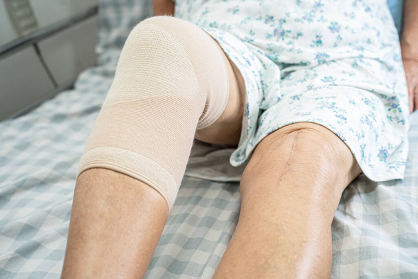 Asiatische Seniorin oder ältere Dame mit Knieschmerz im Bett auf der Krankenstation, gesundes starkes medizinisches Konzept. - Foto, Bild