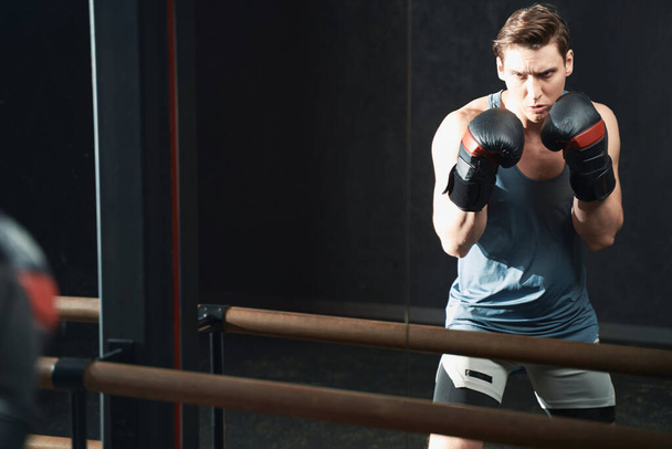 Serious determined young athletic male in boxing gloves standing in fighting stance - Φωτογραφία, εικόνα