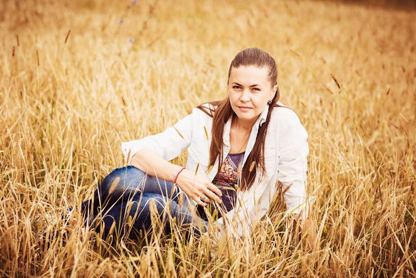 Portrait of a confident authentic young woman sitting in a field in the countryside - Fotó, kép
