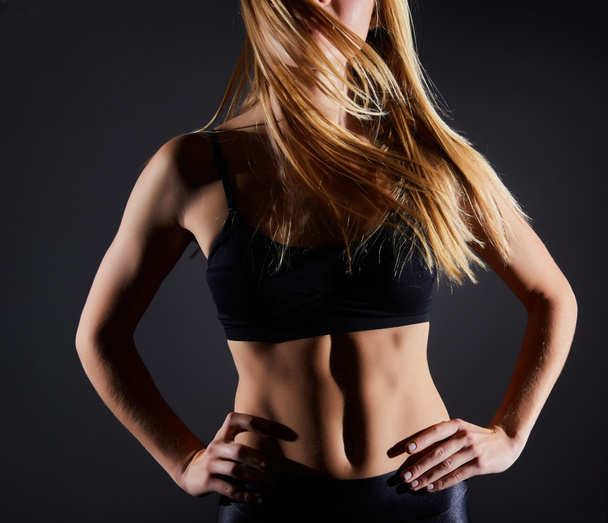 Sportowa młoda blondynka w odzieży sportowej pokazuje mięśnie na czarnym tle. Wielki atletyczny kobiecy organizm - Zdjęcie, obraz