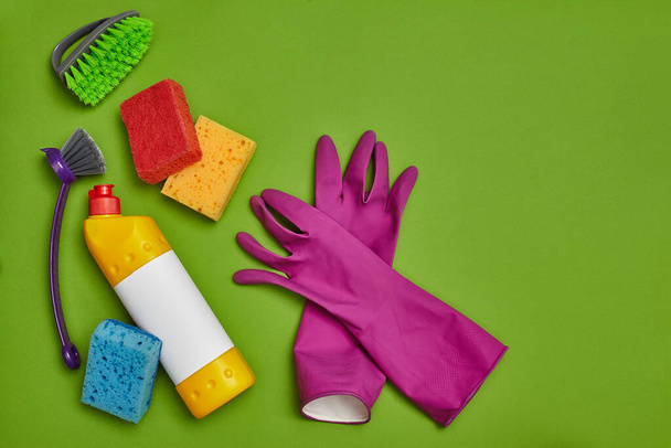 Detergentes modernos y accesorios de limpieza, como: esponjas de colores, guantes de goma púrpura, desinfectante con una etiqueta vacía y dos cepillos modernos sobre un fondo verde. Servicio de limpieza, pequeña - Foto, imagen